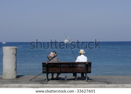 Man is fishing in the Mediterranean Sea. Elderly couple on harbour in Rhodes, Greece.