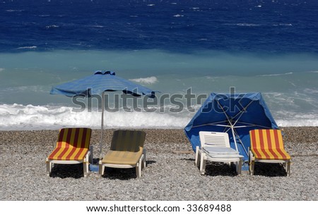 Chairs and umbrellas on the beach close to the rough sea.