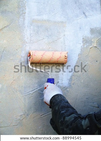 Builder worker painting facade of high-rise building with roller
