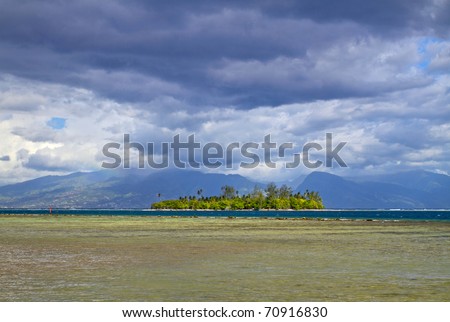 Motu is a small island on the reef, from Moorea island with Tahiti behind the clouds.