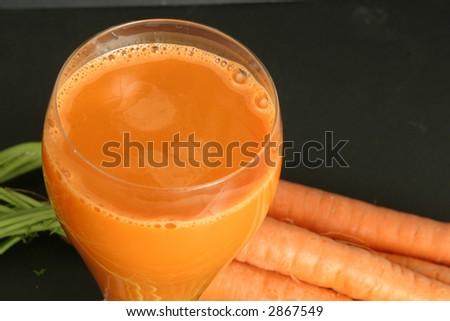Freshly made carrot juice surrounded by carrots isolated on black