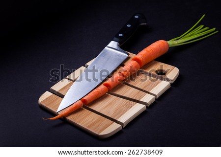Knife with carrot and wooden cutting board and black background