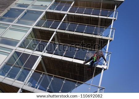 Window cleaner hanging in a rope washing windows in a modern waterfront apartment house