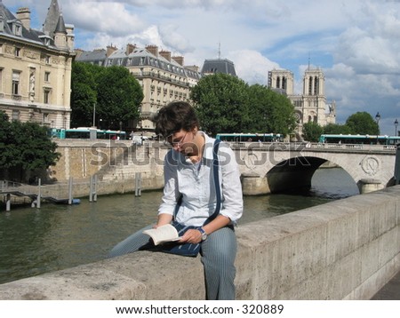 Young adult reading a book near the Seine and Notre Dame in Paris.
