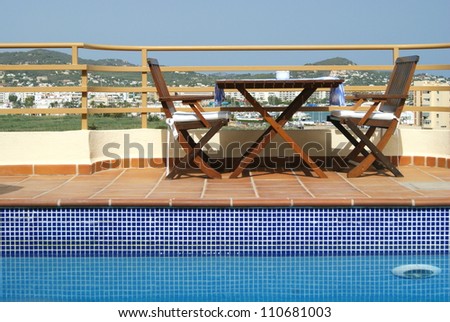 Table and Chairs by Swimming Pool in Roof Garden in Mediterranean City on sunny day