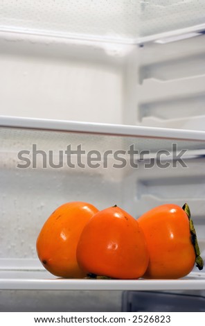 Three persimmons inside fridge, sitting alone on the shelf. Copyspace provided.
