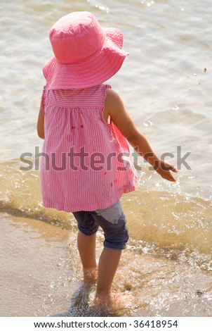 A young girl in pink throwing rocks in a lake
