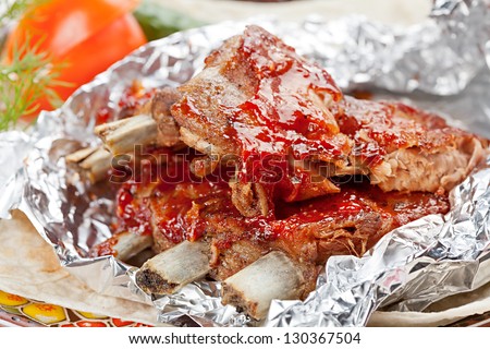 Grilled  ribs with vegetables and sauce on the plate covered in aluminum foil