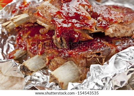 Grilled ribs with vegetables and sauce on the plate covered in aluminum foil