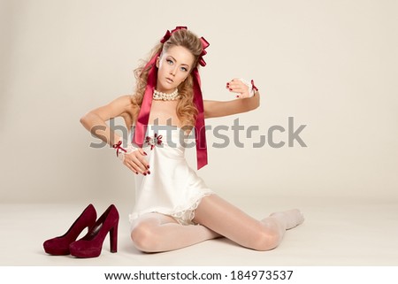 Young woman  in the doll style with red bow and red shoes  sitting on the floor. Studio photography .