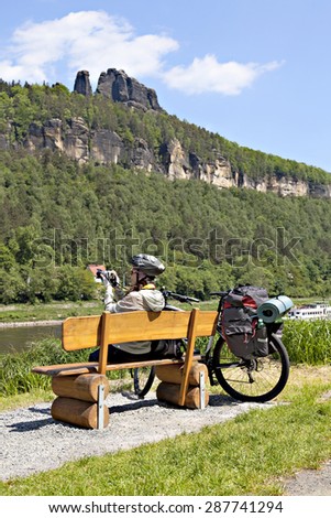 Woman cyclist traveler sitting on the bench and making photo of the landscape around