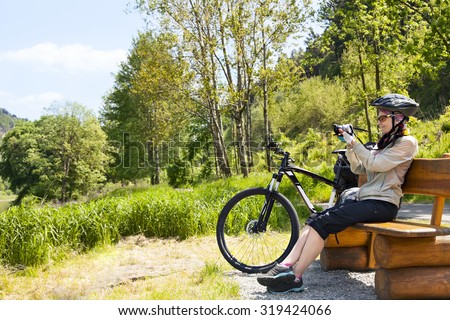 Woman cyclist traveler sitting on the bench and making photo of the landscape around