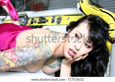 A young heavily tattooed professional model in vintage pin-up style outfit and makeup, leaning out the door of a vintage yellow Buick car