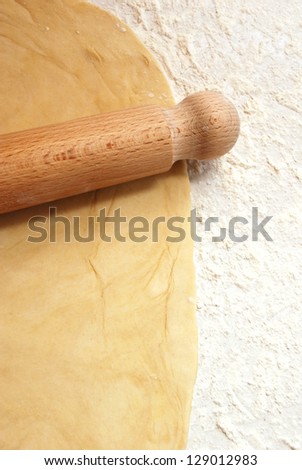 Portrait image of fresh pastry being rolled out on a floured surface with a wooden rolling pin