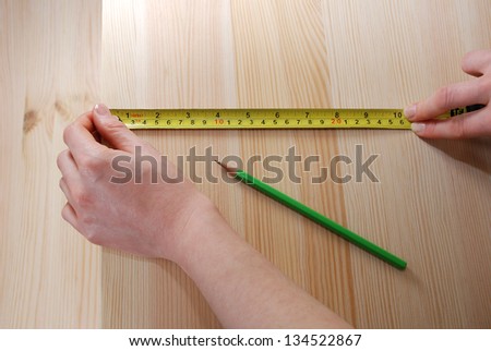 Two hands measuring a wooden board with a steel tape measure in inches and centimetres