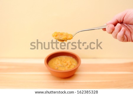 Hand holding spoonful of soup above a bowl on a wooden table with copy space