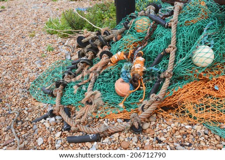 Messy pile of green and orange commercial fishing nets with floats on a beach