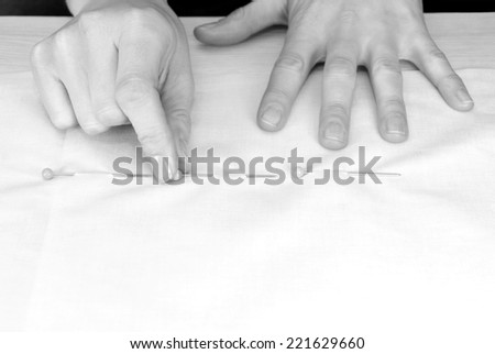 Close up of a woman\'s hands pinning large upholstery pins into plain fabric - monochrome processing