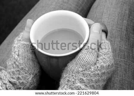 A woman in a warm jumper holding a hot cup of tea or coffee on her lap - monochrome processing