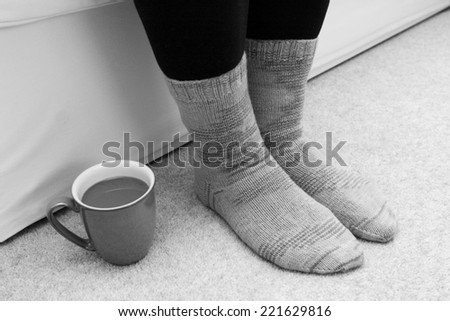 Cup of hot tea or coffee on the floor by a woman\'s feet in knitted socks - monochrome processing