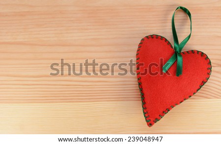Red hand-stitched felt heart decoration with green ribbon on a wooden background with copy space
