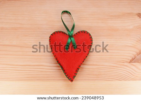 Red felt heart-shaped hanging decoration with green ribbon on a wooden table