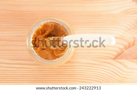 Knife rests in a jar of sticky smooth peanut butter, on a wooden table