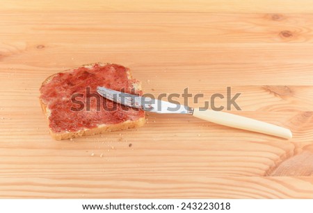 Spreading raspberry or strawberry jam on fresh bread with a knife, resting on a wooden table