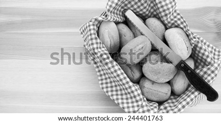 Basket of bread rolls and a knife on a wooden background with copy space - monochrome processing