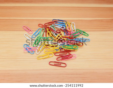 Pile of small coloured paper clips on a wooden background