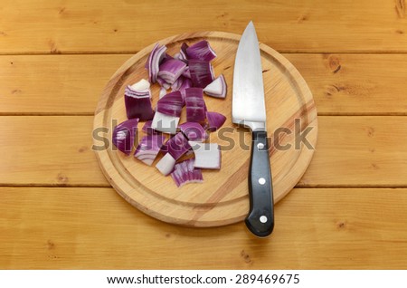 Chopped red onion with a sharp kitchen knife on a chopping board on a wooden table