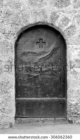 Old studded metal door, decorated with a cross and engraving, in a stone wall in Salzburg, Austria - monochrome processing