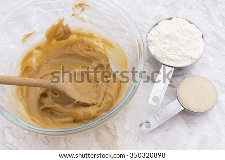 Measuring cups of flour and sugar with a peanut butter mixture in a glass bowl