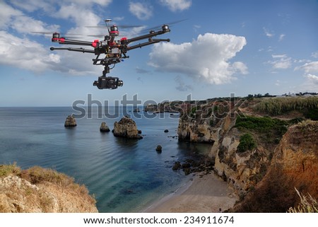 A drone with raised landing gears and a camera flying in beautiful cloudy skies along spectacular sea cliffs with a calm ocean in the background
