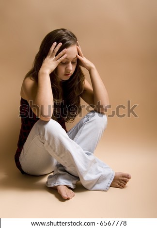 Teenage girl sitting cross-legged on floor in a depressed state.