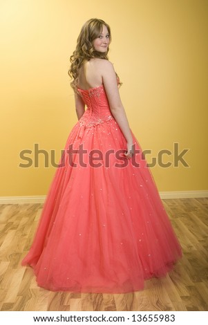 Beautiful teenage girl standing in pink prom dress looking over shoulder. Yellow Background.