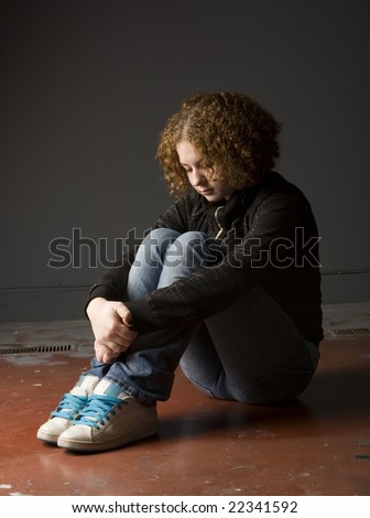 Full length view of teenage girl seated on floor looking depressed.