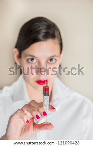 A young attractive women working in medical company holding syringe partly filled with red liquid
