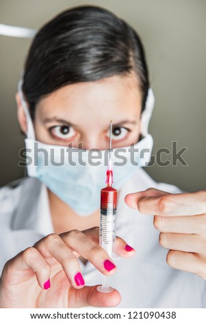 A young attractive women working in medical company holding syringe partly filled with red liquid