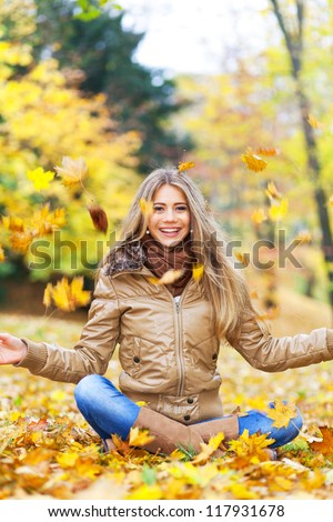 Young woman surrounded by autumn leaves falling