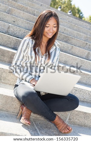 Smiling asian girl sitting on stairs and working on laptop