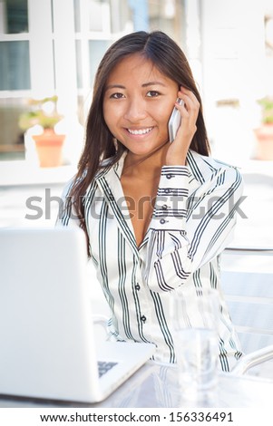Young asian woman in font of a laptop and talking on phone