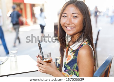 Close up portrait of a smiling asian girl drinking a soda sitting on terrace