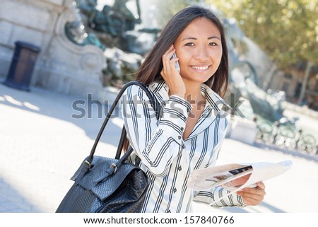Beautiful asian tourist on the phone and holding a city tour map