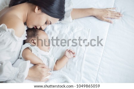 Close up portrait of beautiful young asian mother kissing her newborn baby sleep in bed. Healthcare and medical love lifestyle mother\'??s day concept