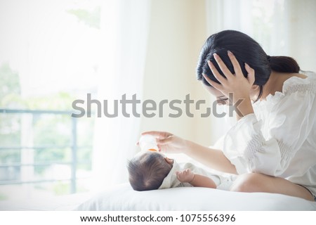 Asian Mother nursery feeding bottle of formula milk to newborn baby in bed suffering from post natal depression. Health care single mom motherhood stressful concept.