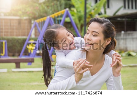 Portrait of happy asian mother and daughter. Asian woman and little toddler girl cuddling and hugging in the playground park. Happy family green spring or summer mother’s day together concept
