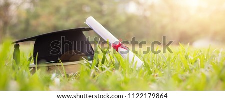 Closeup certificate paper and black cap on green grass spring time in the outdoor park. Education happy success achievement graduated celebrate graduate day concept panoramic background banner