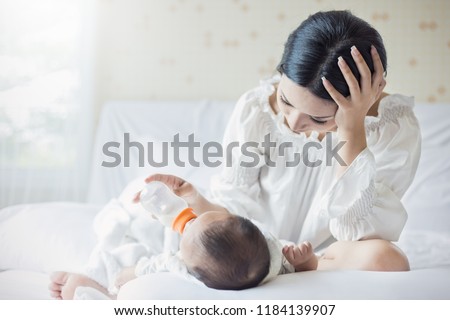 portrait of Asian mother nursery feeding bottle of formula milk to newborn baby in bed suffering from post natal depression. Health care single mom motherhood stressful concept.