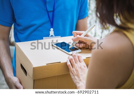 Woman appending signature sign on smartphone after accepting receive a delivery of boxes from delivery man, woman sign on the box, receive delivery concept